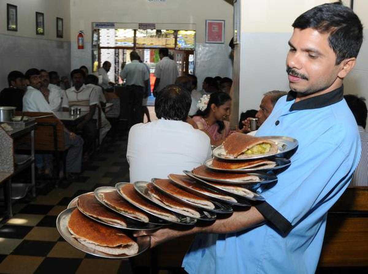 Server carrying multiple plates of masala dosa inside Vidyarthi Bhavan Basavanagudi Bengaluru