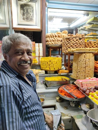 Sweet shop staff smiling inside Guru Sweet Mart in Devaraja Mohalla, Mysuru, with traditional Indian sweets displayed