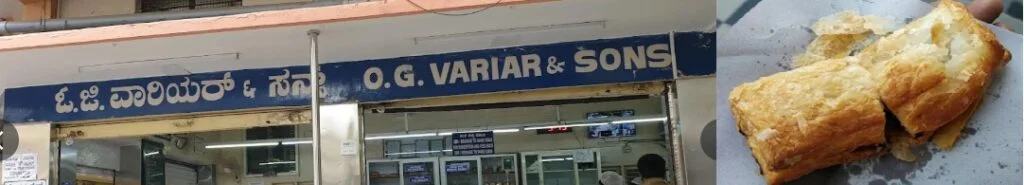 Exterior view of O.G. Variar & Sons bakery in Rajajinagar Bengaluru with the shop signage and freshly baked vegetable puffs displayed.