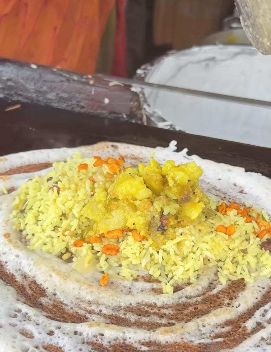 Cook preparing crispy dosa with ghee and stuffed with chitrana and aloo palya on hot tawa at Mahesh Hotel Doddaballapur.