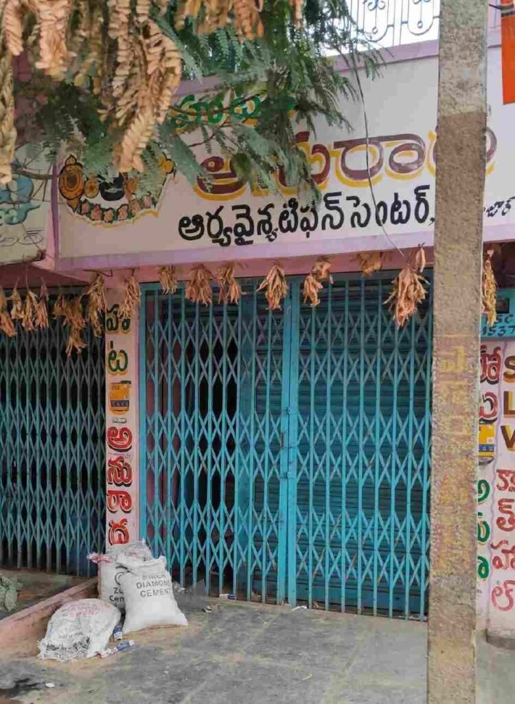 Front view of Anuradha Hotel with closed blue metal shutters and Telugu signboard above the entrance.