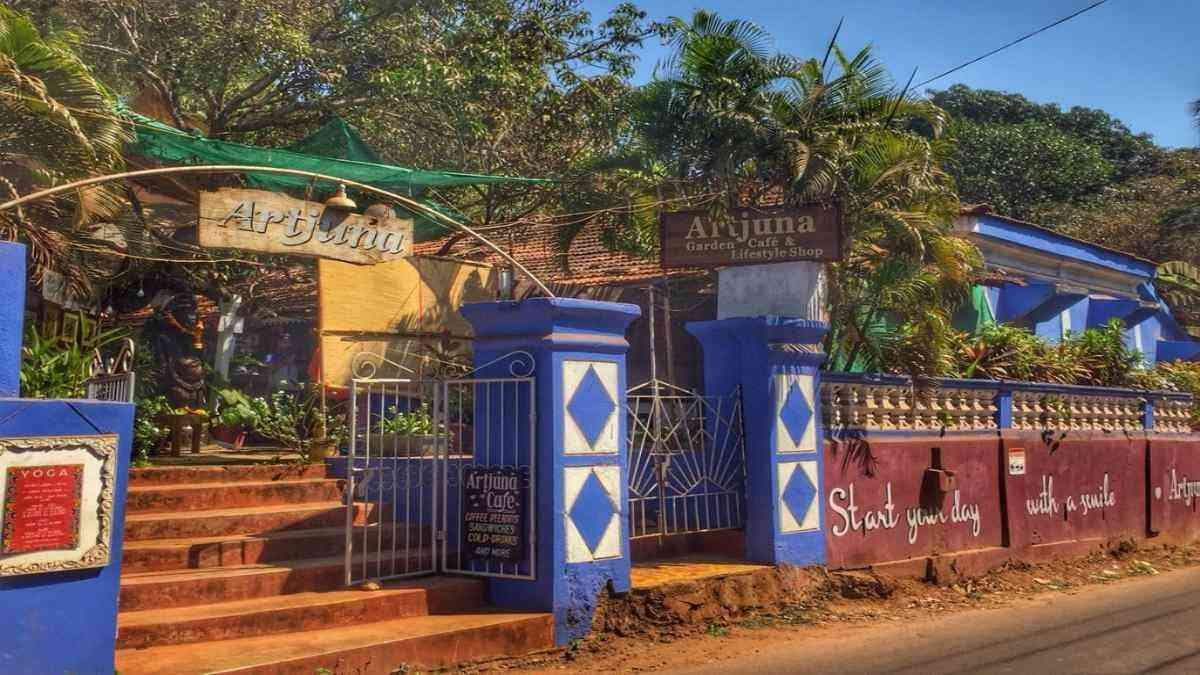 Entrance of Artjuna Café in Goa surrounded by greenery with colorful gate and rustic design