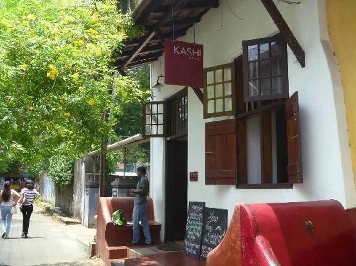 Exterior of Kashi Art Café in Kochi with white walls, wooden windows, and greenery