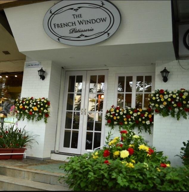 Entrance of The French Window Patisserie Pune decorated with flowers and white facade