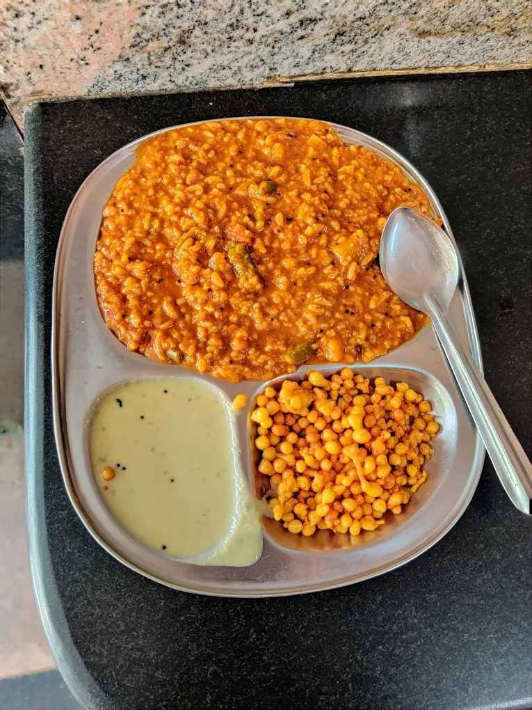 Bisi Bele Bath served at S N Refreshments JP Nagar Bengaluru with boondi and coconut chutney on a stainless steel plate.