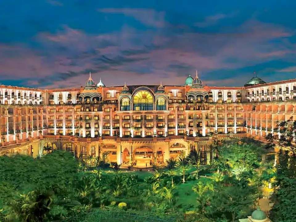 Night view of The Leela Palace Bengaluru showcasing royal architecture, illuminated building, and lush green gardens.