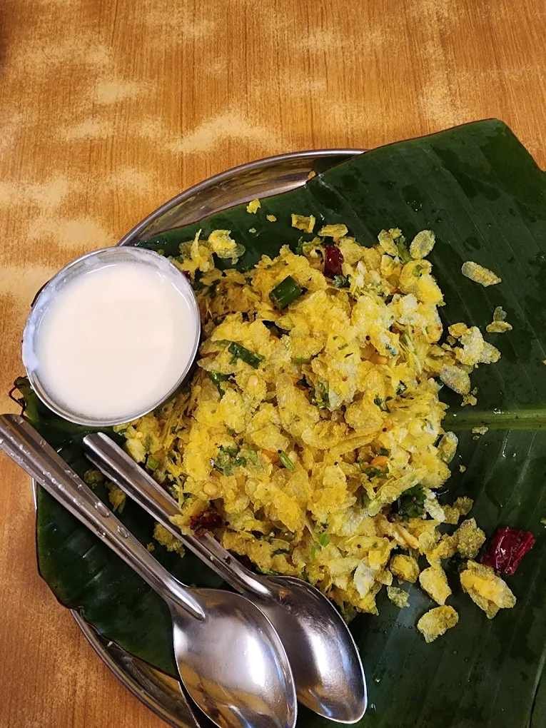 Avalakki Mosaru served on a banana leaf with a side of fresh curd, garnished with curry leaves, green chilies, and spices at Meenakshi Bhavan.