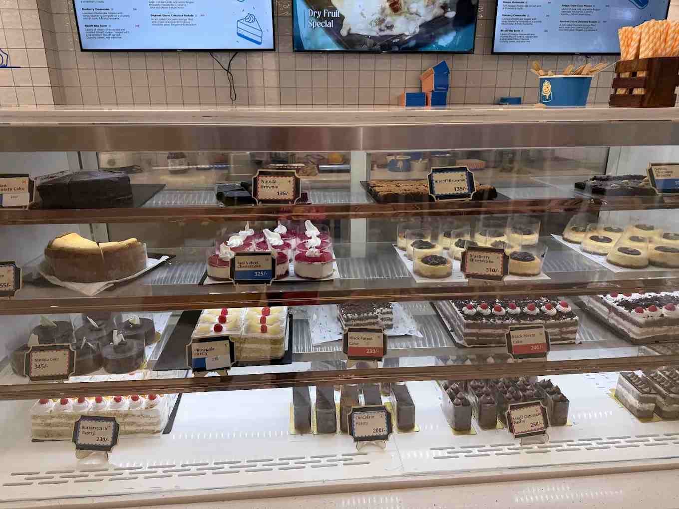 Dessert display counter inside Lakeview Milkbar Bengaluru featuring cakes, pastries, and cheesecakes