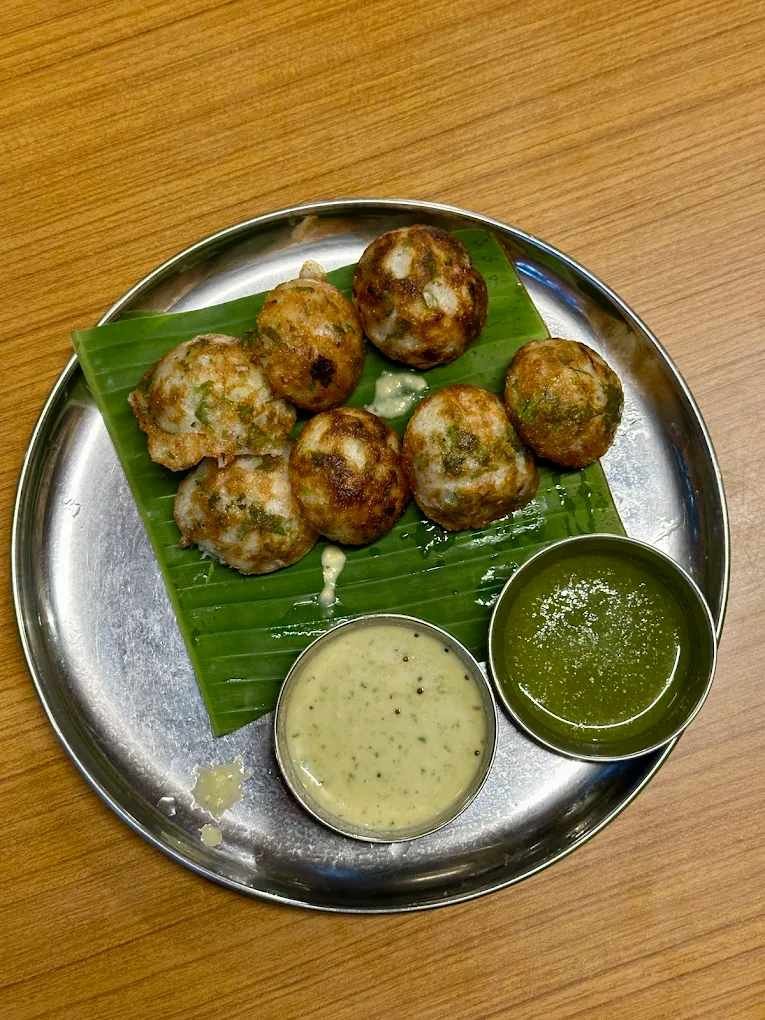 Plate of freshly prepared Paddu served on a banana leaf with coconut chutney and green chutney at Meenakshi Bhavan.