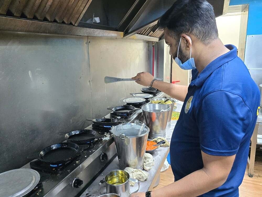 Chef preparing authentic Mulbagal Dosa on traditional tawas inside the kitchen of Prasad Hotel in Mulbagal.